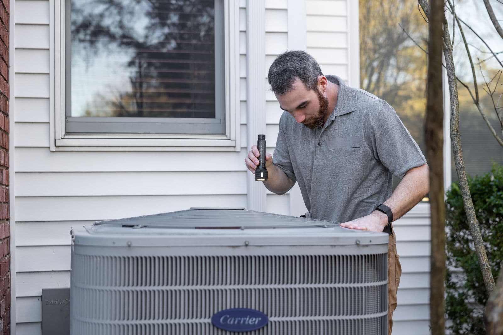 HVAC technician inspecting an outdoor condenser unit at a home